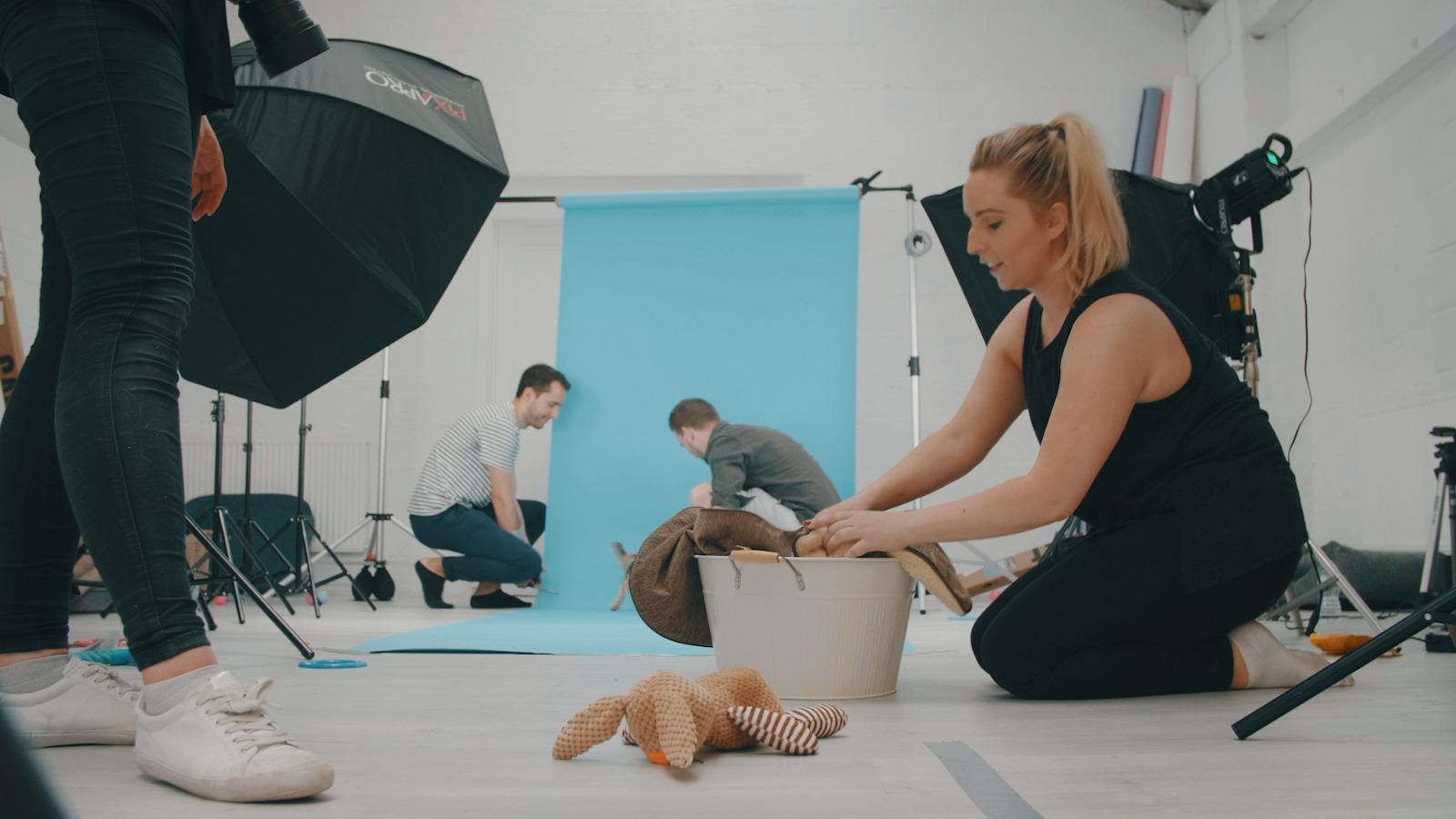 Nomadic UK – On set with a dog bed video shoot, producer in the foreground setting up one of the looks Nomadic UK - stylist setting up a look on a video shoot in a studio with a blue backdrop